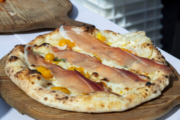 street food, Neapolitan tradition, mozzarella pizza and Piennolo cherry tomatoes with raw ham placed on top cooked in a wood oven