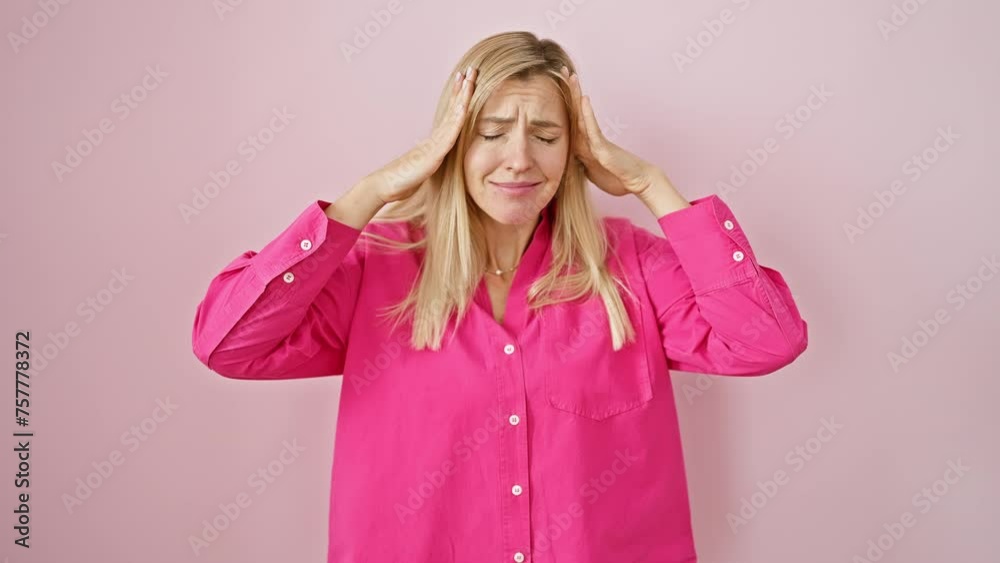 Sticker stressed-out blonde woman grips head in pain over pink backdrop, suffering from a headache and migra