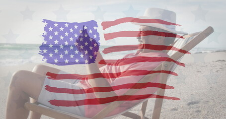 Image of flag of united states of america over senior biracial man using tablet on beach