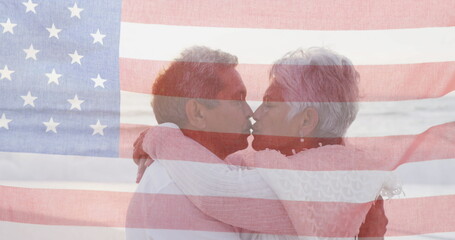 Image of flag of united states of america over senior biracial couple embracing on beach