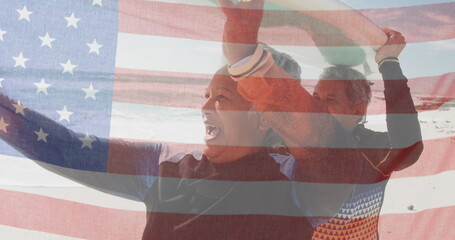 Image of flag of united states of america over senior biracial couple with surfboard on beach