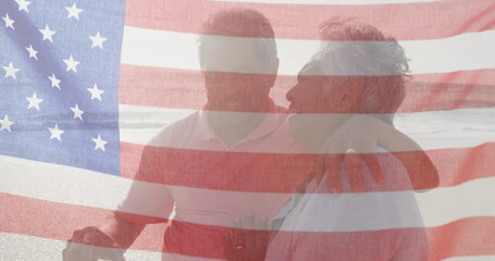 Fototapeta na wymiar Image of flag of united states of america over senior biracial couple kissing on beach