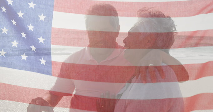 Image of flag of united states of america over senior biracial couple kissing on beach