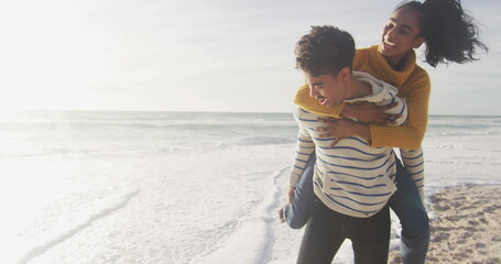 Biracial woman gives piggyback ride to young biracial man on a beach