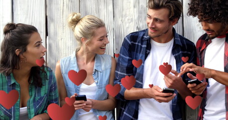 Digital composite of a group of teens leaning on a wooden fence texting and digital hearts flying in