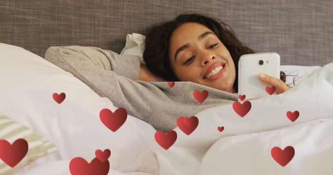 Hispanic woman smiles and texts in bed with digital hearts around her in 4k.