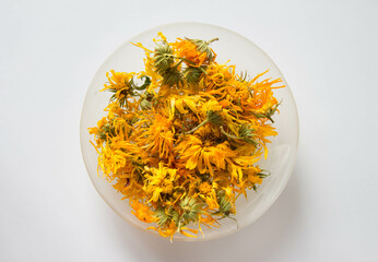 Dry calendula flowers in glass bowl on white background. Organic medicinal herbs. Top view.