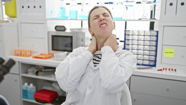 A distressed woman in a laboratory setting clutches her neck in apparent discomfort or stress, surrounded by scientific equipment.