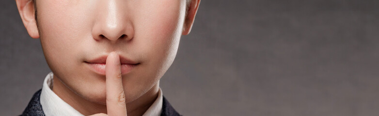 An oriental man in a business suit holds his index finger to his lips. - obrazy, fototapety, plakaty