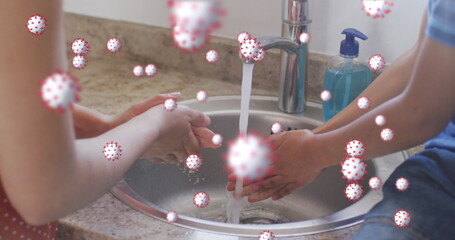 Image of coronavirus cells over caucasian mother with son washing hands at home