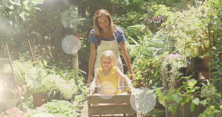 Spots of light against caucasian mother carrying her daughter in the garden cartin the garden