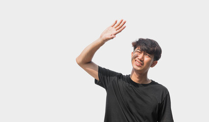 A young Asian man in his 20s wearing a black t-shirt is using his hands to block the sunlight that hits him, isolated on a gray background. The concept of facing the sun or hot weather