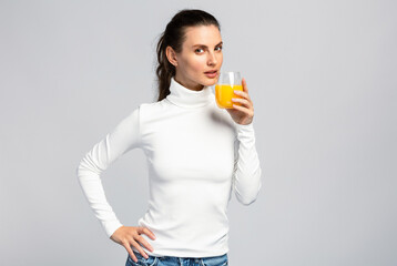 Beautiful young woman drinking a glass of orange juice, healthy lifestyle, on light grey studio background