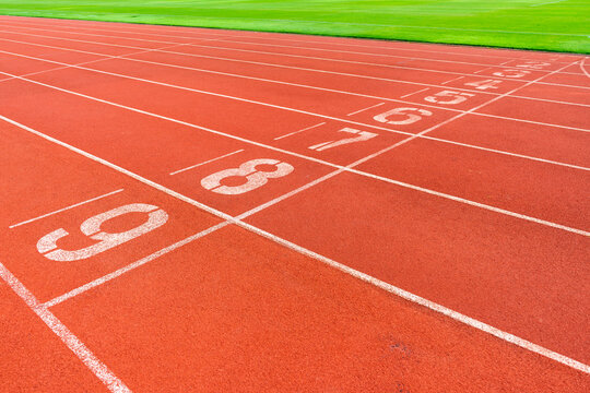 Red running track with green grass in stadium. Athletic competitions starting line positions from one to nine. © Jitti