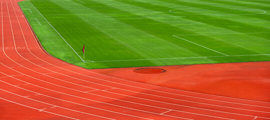 Red running track with green grass in stadium. Outdoor track and field stadium runway.
