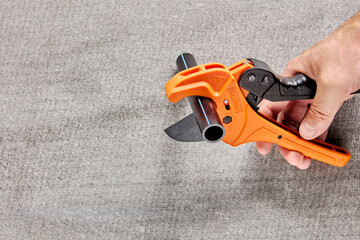 Plumber cuts piece from plastic pipe using ratchet pipe cutter.