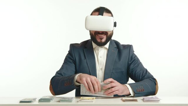 A modern businessman in a sleek blue suit is deeply engaged with virtual reality glasses, counting a stack of bills, symbolizing the intersection of traditional finance and cutting-edge technology.