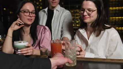 Bartender takes away empty glass serving new drink to young woman. Lady chats with friends enjoying free time after work in bar
