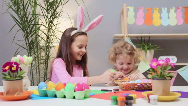 Easter egg painting party. Messy egg dyeing fun. Decorate eggs for Easter. Egg painting with kids. Little girls decorating eggs in vibrant colors in light festive room interior