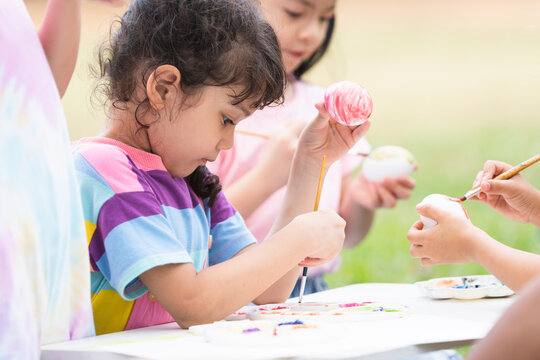 Happy group of cute little children girls painting Easter eggs together. kids holding painting brush, painting watercolor on egg while playing outdoors at park