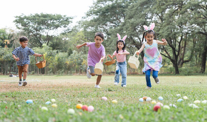 Happy group of diverse cute little children hunting Easter eggs, wearing bunny ears. kids holding...