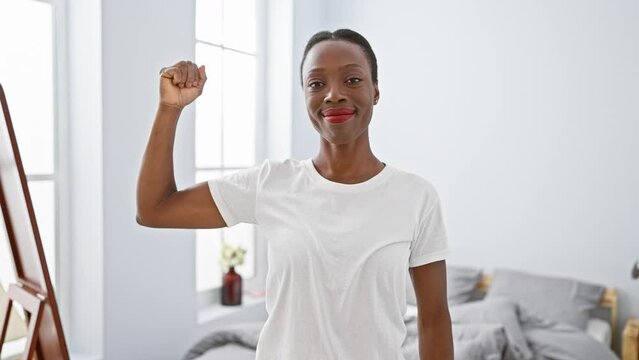 Strong african american woman flexing arm muscle in bedroom, living a healthy lifestyle at home, proud of her power and fitness