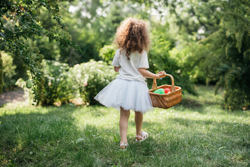 Easter egg hunt. Girl child Wearing Bunny Ears Running To Pick Up Egg In Garden. Easter tradition. Baby with basket full of colorful eggs. - 757825501