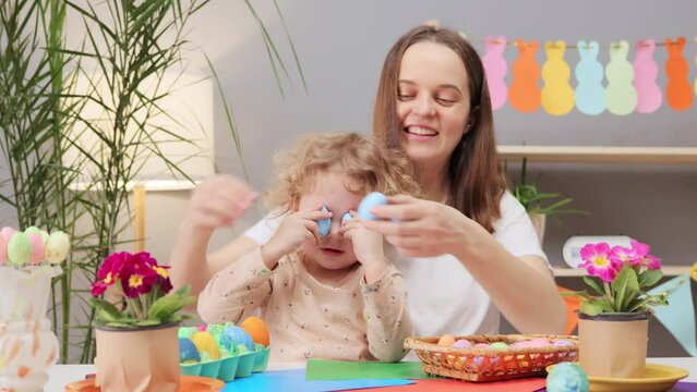 Joyful young woman with little daughter painting Easter eggs in festive home interior engaging in meaningful Easter traditions and rituals with loved family