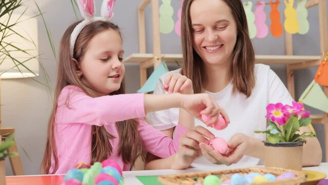 Overjoyed family spending time together while sitting on table and painting Easter eggs in festive home interior creating festive atmosphere for holiday preparation