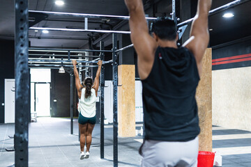 Group of attractive young male and female adults doing pull ups on bar in cross fit training gym