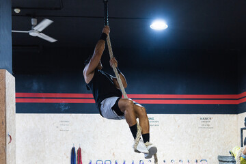Male athlete or sportsman climbing rope at gym.