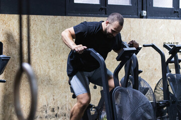 Fototapeta na wymiar Man using air bike for cardio workout at cross training gym.