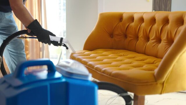 A man performs wet cleaning on a sofa, employing a specialized professional washing vacuum cleaner for effective and thorough cleaning.
