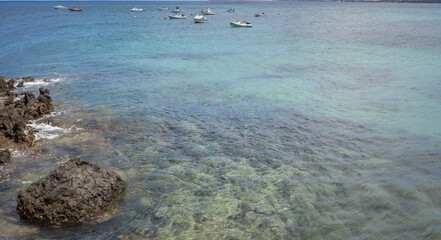 Seascape. Group of boats anchored near the pier. Turquoise Atlantic Ocean. Big white clouds. Village of Arrieta. Lanzarote, Canary Islands, Spain
