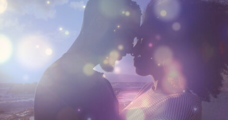 Glowing blue spots of light over african american couple embracing each other on the rocks near sea