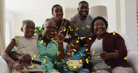 Image of gold confetti over multi generation family watching sports celebrating at home