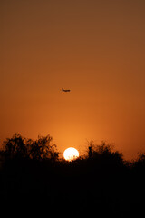 Silhouette of a plane flying against orange sky at sunset