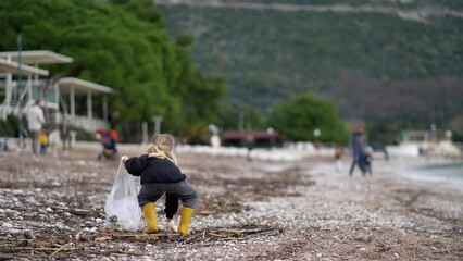 A young girl is collecting litter at the beach, helping to protect the water and plant life. Encouraging people to keep nature clean and beautiful