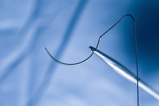 Closeup photo of a needle holder and half circle needle with suture during operation.