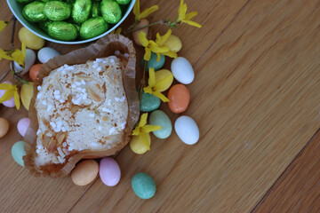 Sweet Easter cake named Colomba Pasquale with colorful chocolate eggs and yellow Forsythia flowers . Italian traditional pastry on wooden table
