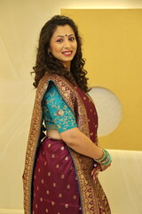 Gujarati woman wearing Saari in Gujarati stlye. Model is posing with a side pose and have smiling face and cirly hair. she has wore bindi and lovely bangles. Green and purple saari is just beautiful