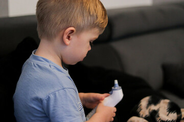 Toddler boy holding and looking at a digital thermometer, sitting on a couch, blurry background