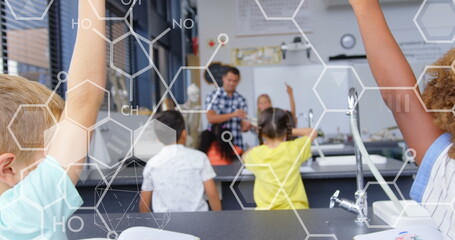 Image of chemical icons over diverse schoolchildren raising hands in classroom