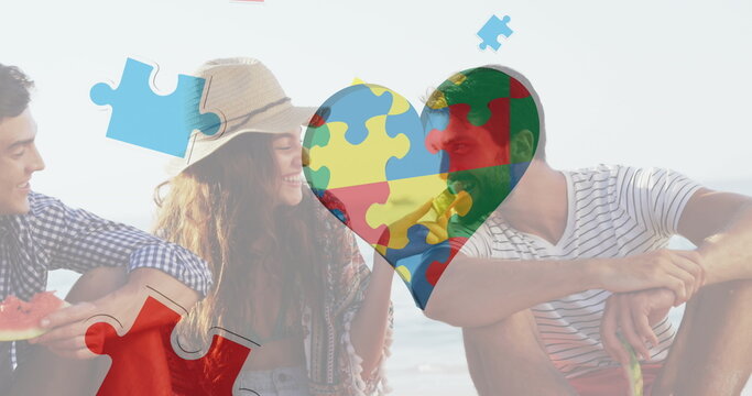 Image of colourful puzzle pieces heart over happy friends at summer beach party
