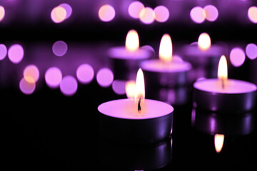 Burning violet candle on black background, closeup. Funeral attributes