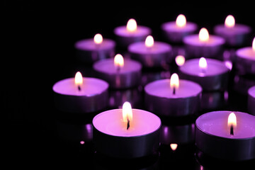 Obraz na płótnie Canvas Beautiful burning violet candles on black background. Funeral attributes