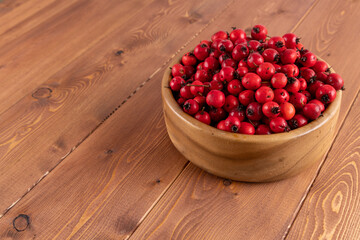 red hawthorn berries in wooden bowl on flat wooden surface.