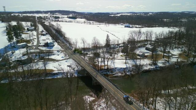 Drone image of creek with bridge over it. Farm fields with snow.