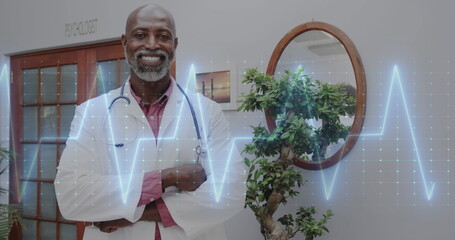 Image of cardiograph over happy african american male doctor with stethoscope