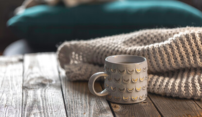 Cozy background with shiny gray cup and knitted element on wooden background.